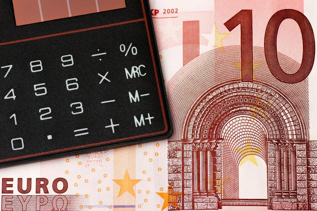 Schwarzer Taschenrechner mit Prozenttaste liegt schräg auf einem rot-weißen Zehn-Euro-Schein, Nahaufnahme von oben