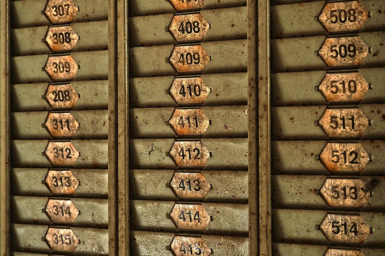 Alter Metallhalter für Stempelkarten an einer Wand, die Fächer tragen nummerierte Messingschilder der Reihen 300, 400 und 500